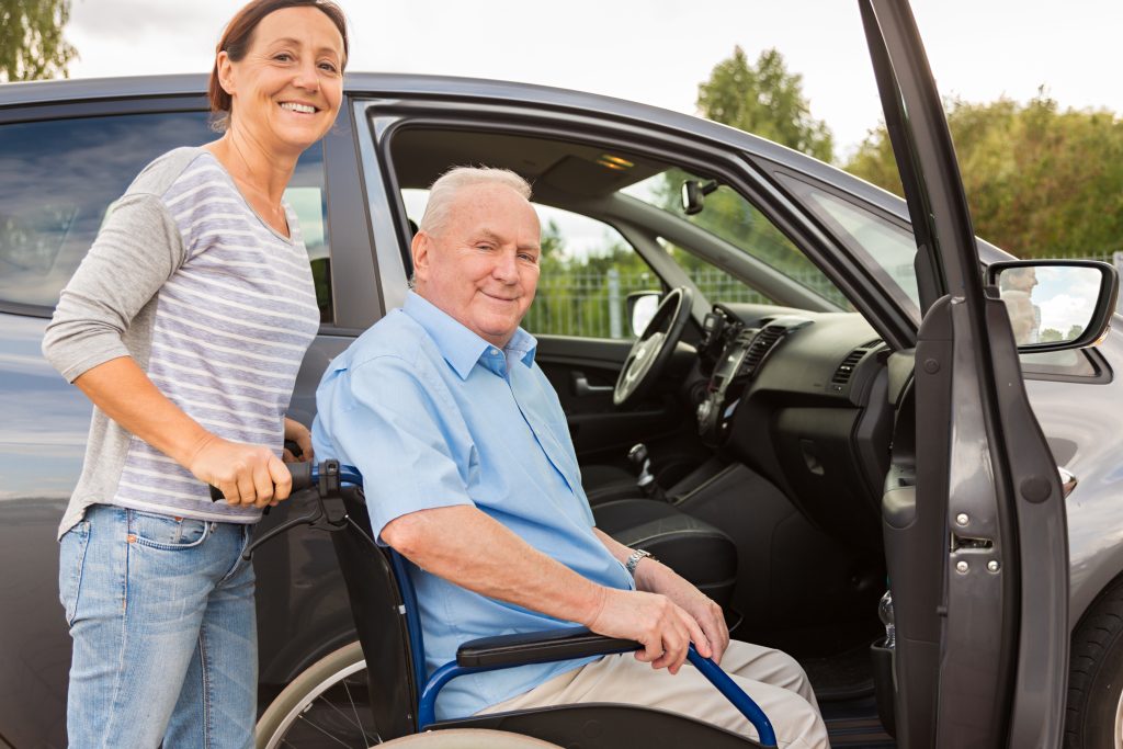 Caregiver helping elderly man with wheelchair at vehicle