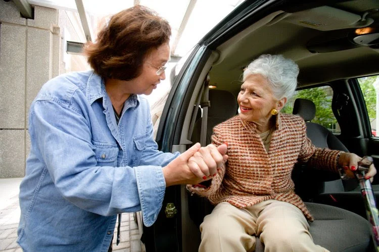 Caregiver helping senior woman exit a vehicle